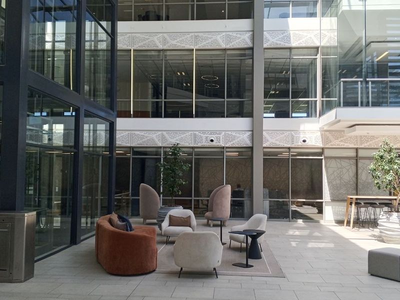A modern, light-filled office atrium featuring expansive glass curtain walls, high ceilings, and high-quality tiled flooring in a professional corporate environment.