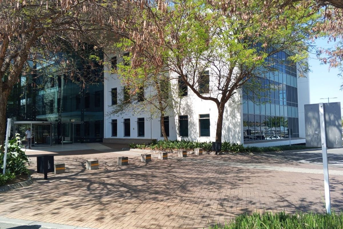 Modern office building exterior featuring a glass curtain wall facade, paved entrance area, and professional landscaping.