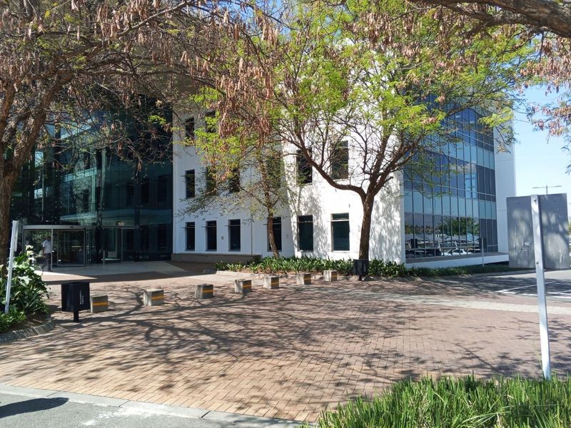 Modern office building exterior featuring a glass curtain wall facade, paved entrance area, and professional landscaping.