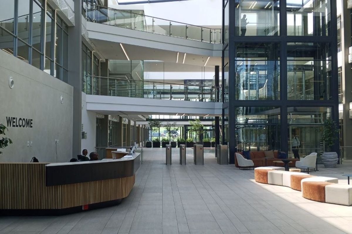 Modern office building atrium featuring a glass elevator, multi-level walkways, high ceilings with skylights, and a professional reception area.