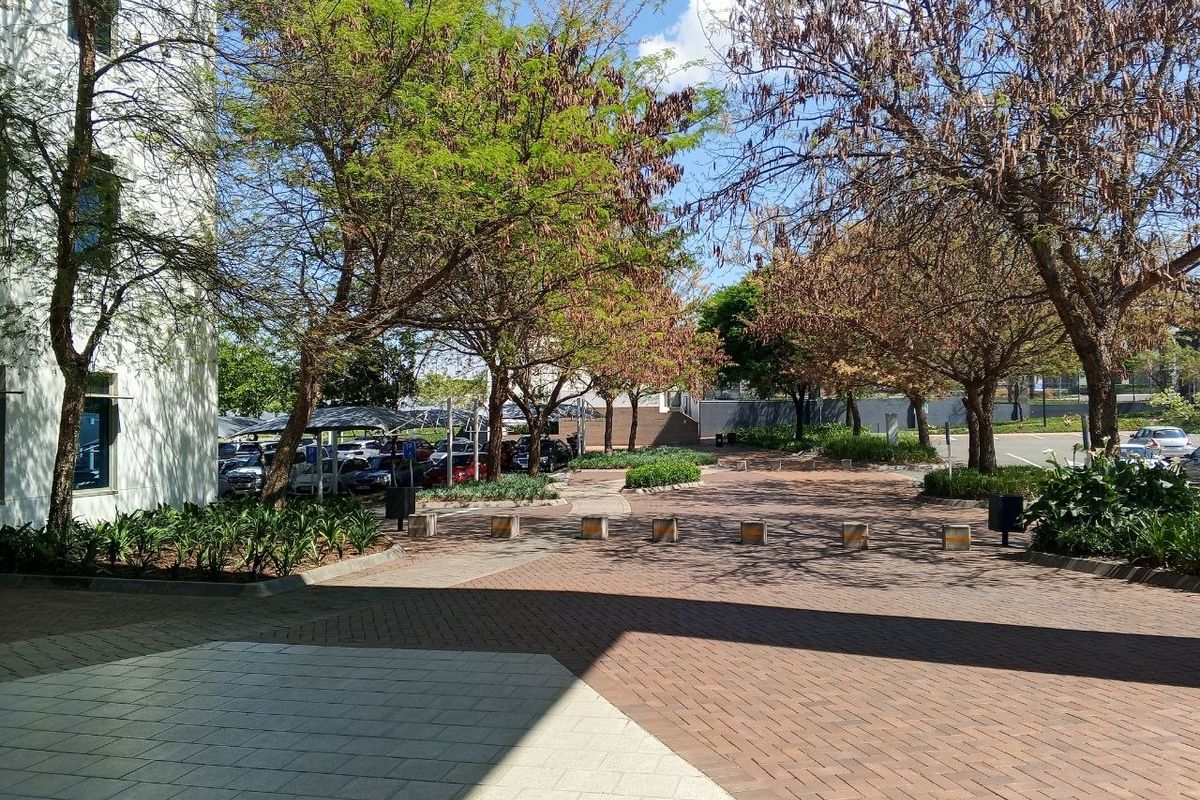 A well-maintained office exterior featuring a paved driveway, landscaped garden areas, and covered parking facilities.