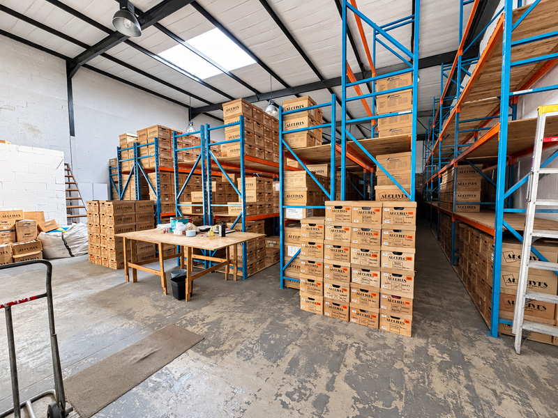 Industrial warehouse space featuring high ceilings with exposed steel trusses, skylights, and extensive heavy-duty steel racking systems on concrete flooring.