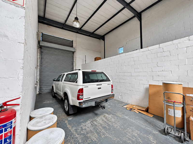 Industrial garage space featuring high ceilings with exposed steel trusses, a large roller shutter door, and durable painted concrete flooring.
