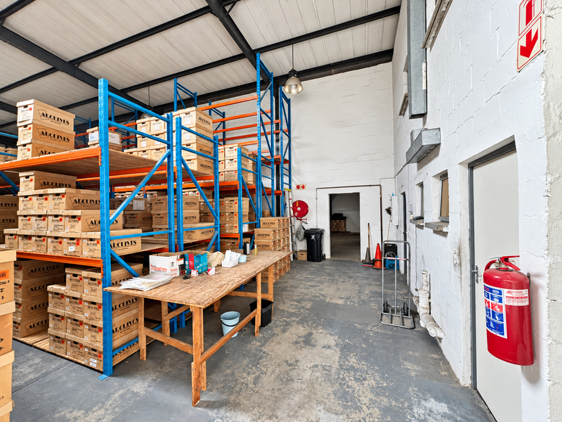 Industrial warehouse space featuring high-clearance steel racking, exposed roof trusses, and durable concrete flooring, equipped with essential fire safety infrastructure.