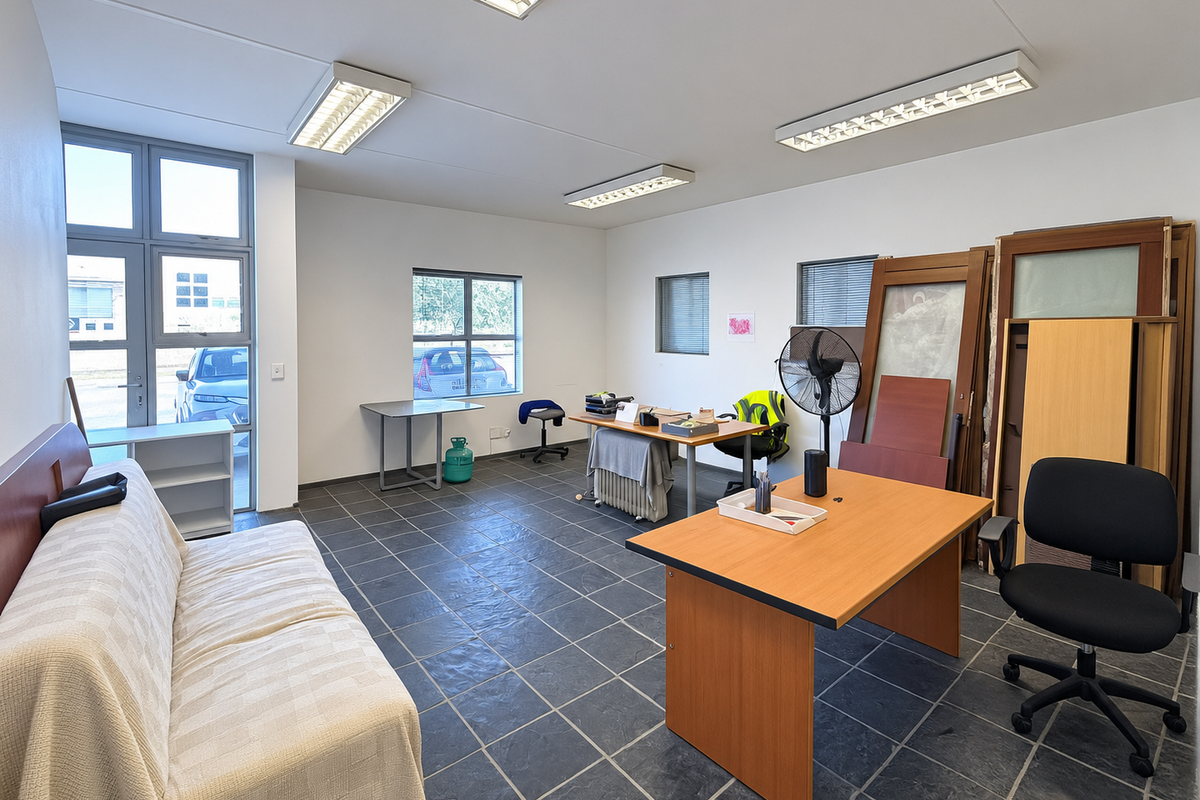 A functional office space featuring tiled flooring, ample natural light through aluminium windows, and overhead fluorescent lighting, suitable for a professional work environment.