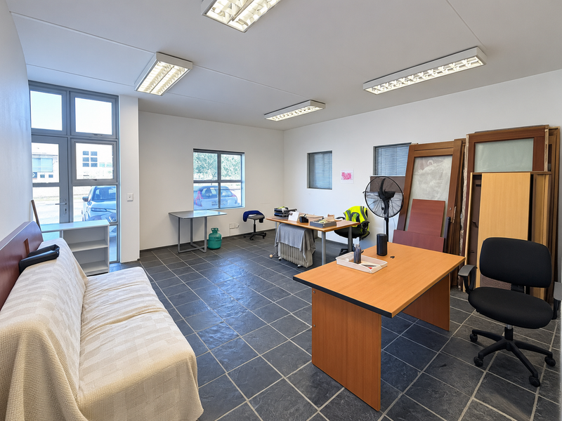 A functional office space featuring tiled flooring, ample natural light through aluminium windows, and overhead fluorescent lighting, suitable for a professional work environment.