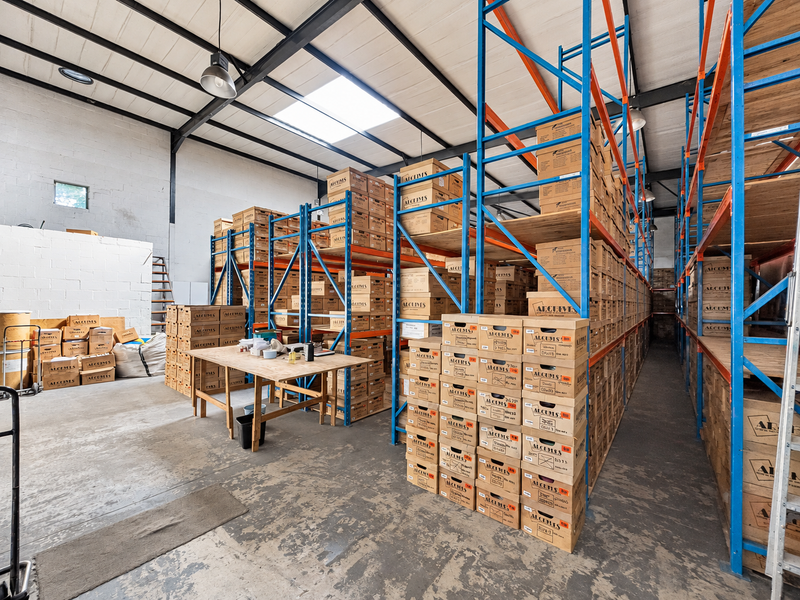 Spacious industrial warehouse featuring high ceilings with exposed steel trusses, skylights, and extensive built-in steel racking systems for organized storage.