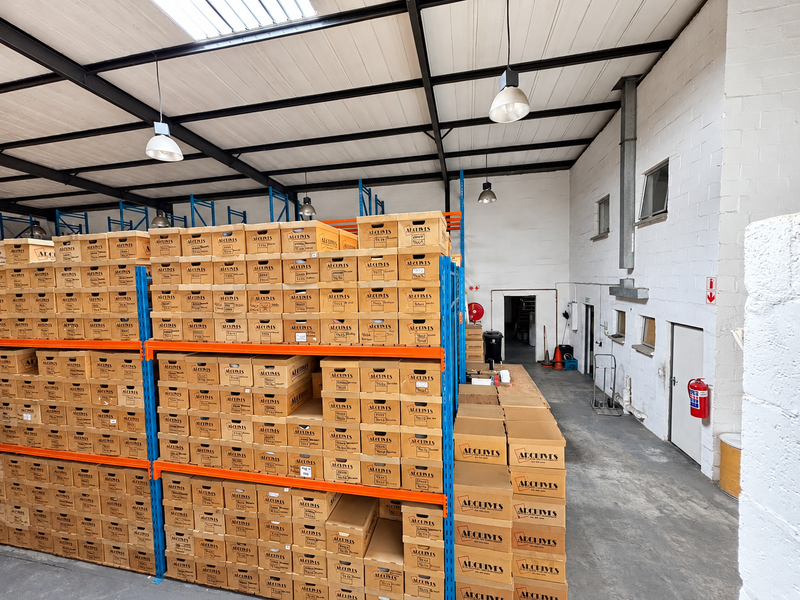 Industrial warehouse space featuring high ceilings with exposed steel trusses, skylights, concrete flooring, and extensive built-in steel racking systems for storage.