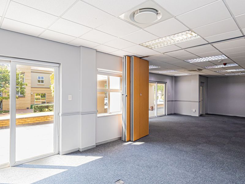 Spacious open-plan office area featuring a flexible folding partition wall, suspended ceilings with recessed lighting, and large sliding glass doors providing natural light.