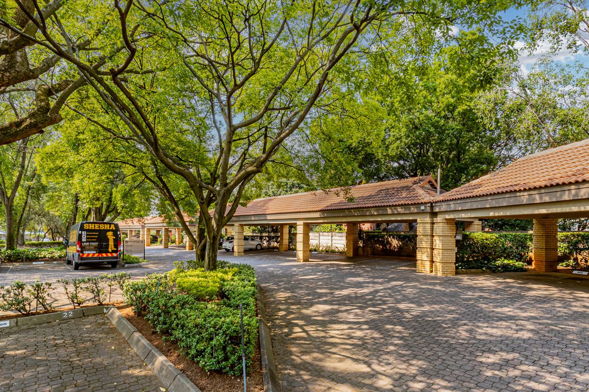 A well-maintained office exterior featuring covered parking bays with brick pillars, a paved driveway, and mature trees in a landscaped setting.
