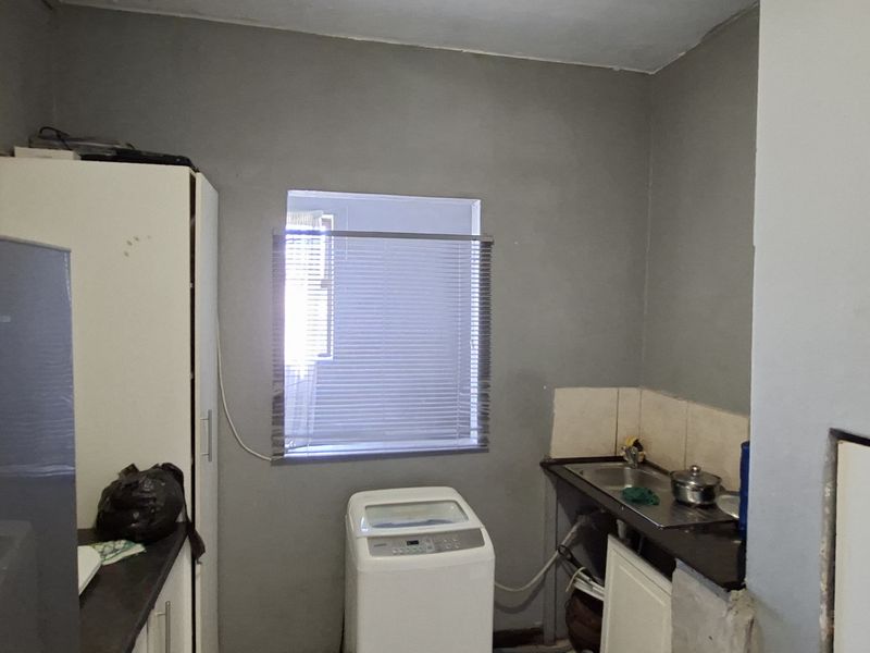 A functional laundry area featuring a stainless steel sink, tiled splashback, and dedicated space for laundry appliances.