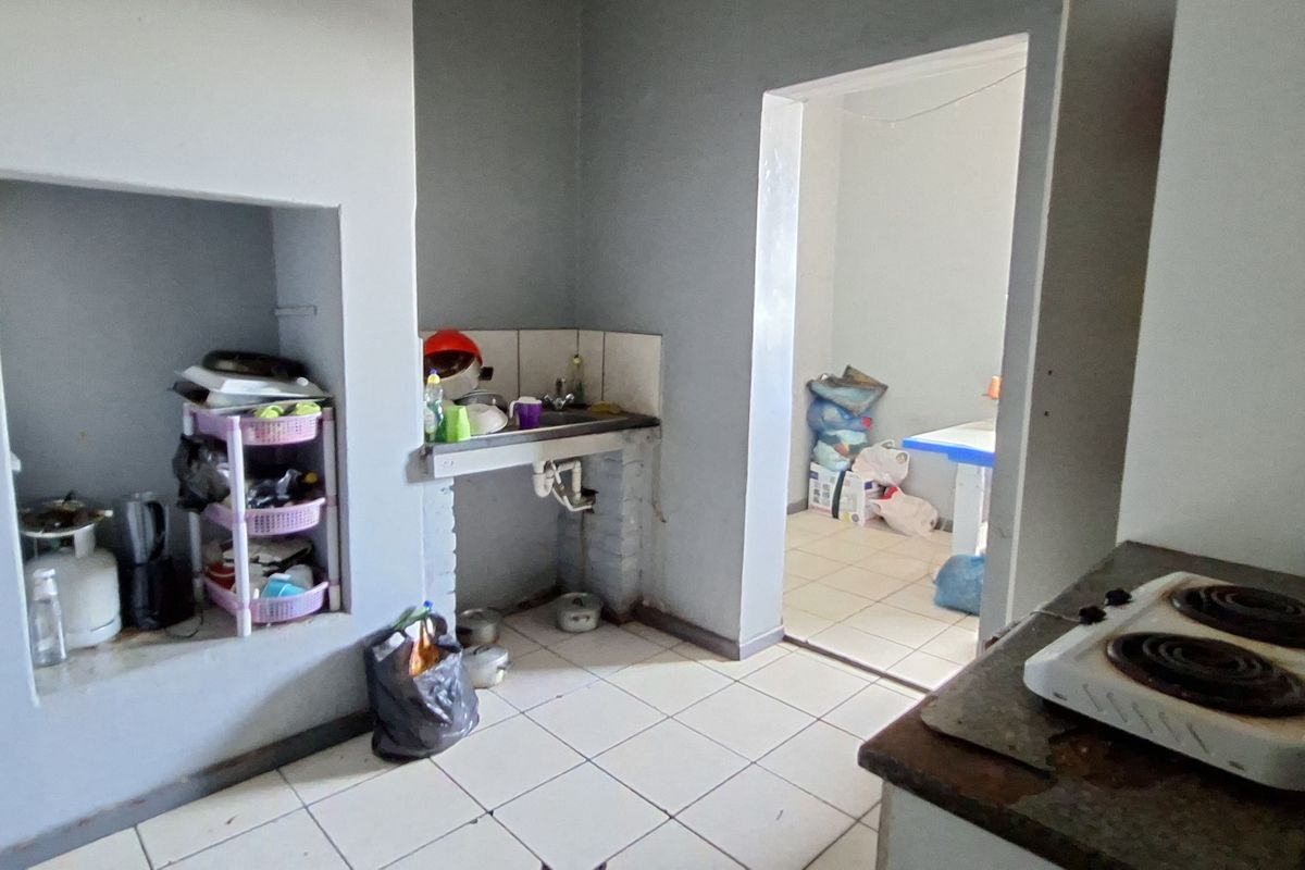 A basic kitchen area featuring tiled flooring, a built-in sink, and an alcove, requiring significant renovation and modernization of finishes.