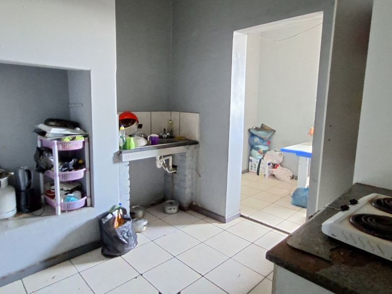 A basic kitchen area featuring tiled flooring, a built-in sink, and an alcove, requiring significant renovation and modernization of finishes.