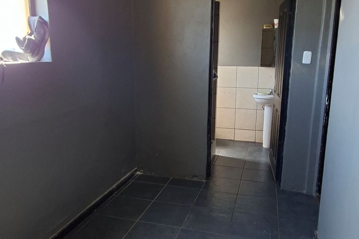 A small, empty bathroom space featuring dark wall tiles, a skylight, and a doorway leading to an adjacent area.