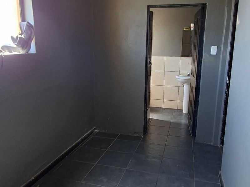 A small, empty bathroom space featuring dark wall tiles, a skylight, and a doorway leading to an adjacent area.