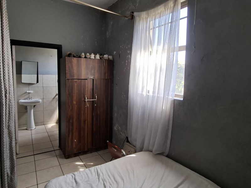 A bedroom featuring tiled flooring and an en-suite bathroom with a pedestal basin. The walls require maintenance and repainting.