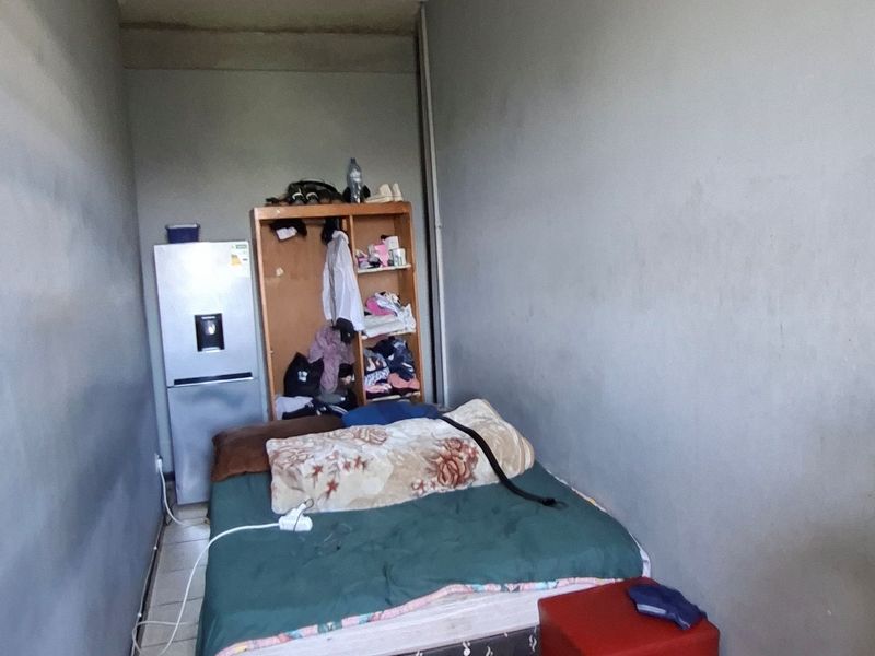 A bedroom featuring tiled flooring and a ceiling light fixture, currently showing signs of wear on the walls.