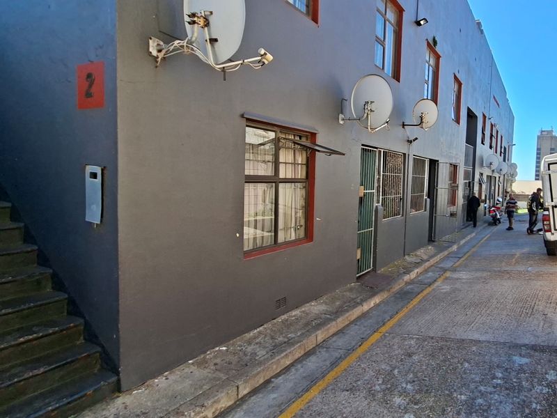 Exterior view of an apartment building facade featuring an external staircase, security gates, and multiple satellite dish installations along the wall.