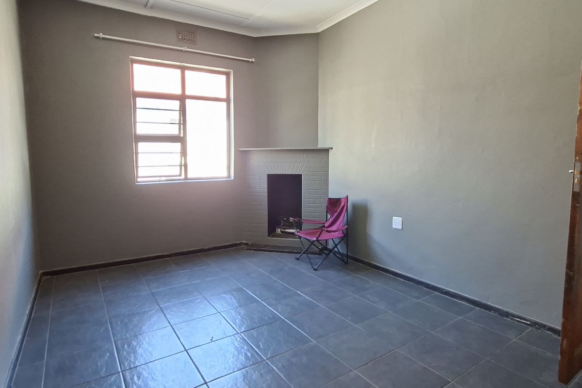 A spacious living room featuring dark tiled flooring, a built-in fireplace, and a window with security bars, offering a blank canvas for interior design.