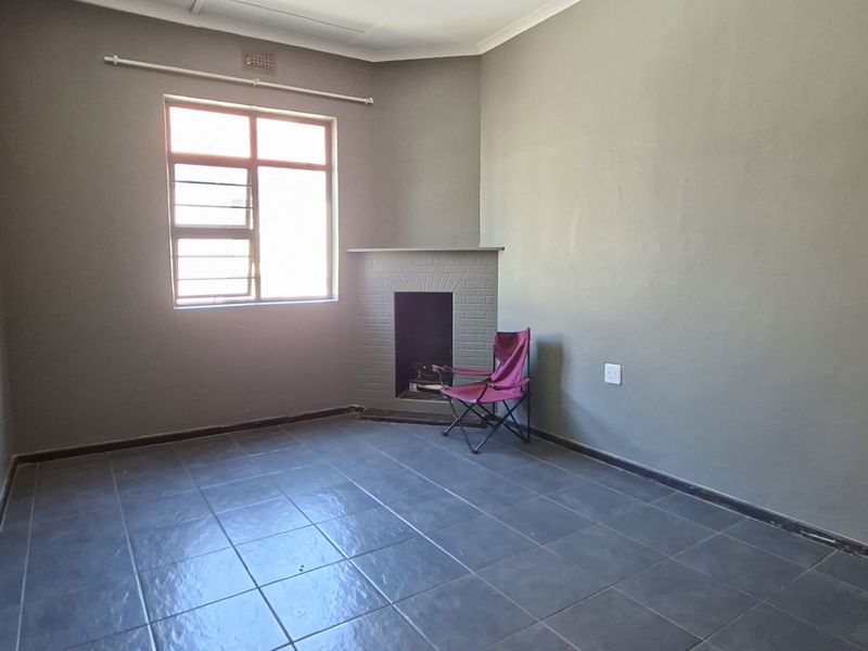 A spacious living room featuring dark tiled flooring, a built-in fireplace, and a window with security bars, offering a blank canvas for interior design.