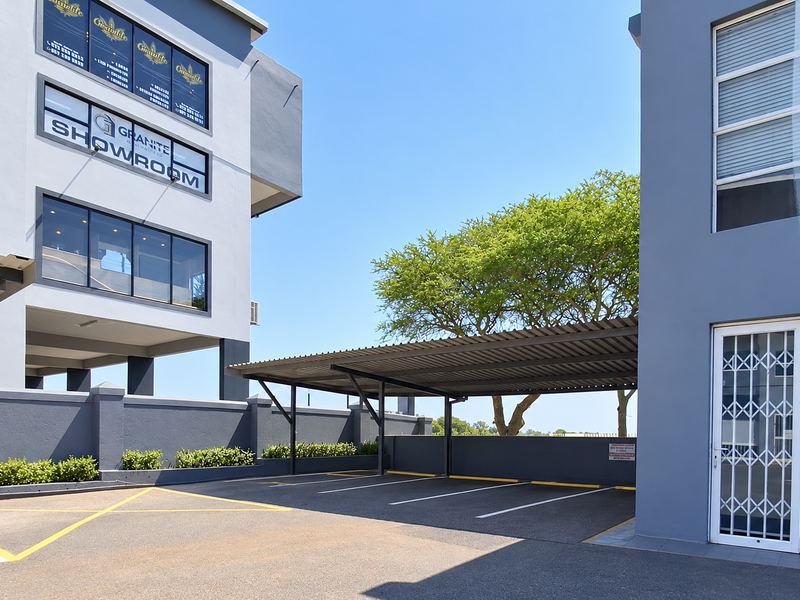 Exterior view of a modern office building featuring a paved parking area with a covered carport and secure access gate.