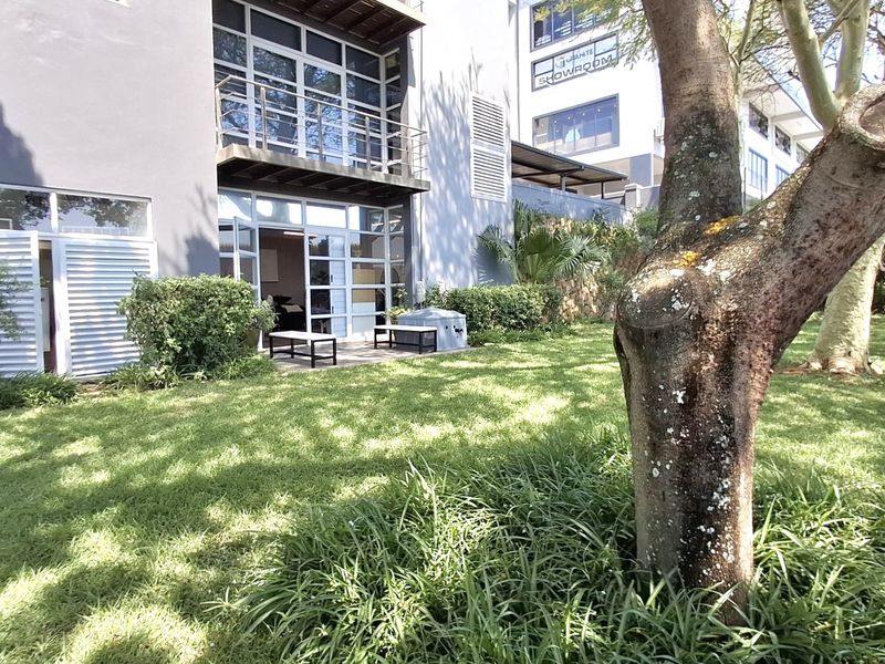 Rear view of the office building featuring a landscaped garden, stone retaining wall, and a balcony with glass sliding door access.