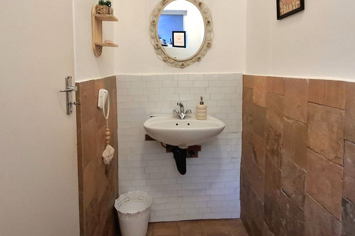 A compact bathroom featuring a wall-mounted basin with a chrome mixer tap, accented by subway tile backsplash and textured stone wall cladding.