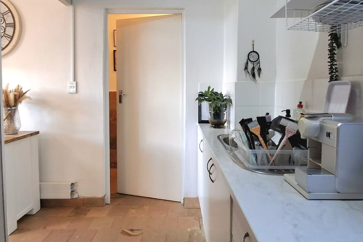 A functional kitchen area featuring white cabinetry, marble-effect countertops, a stainless steel sink, and tiled flooring, with an adjacent doorway leading to another room.