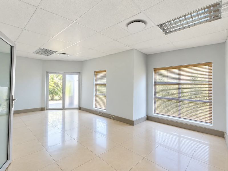 A bright, vacant office space featuring ceramic tile flooring, suspended ceilings with recessed lighting, and large windows with fitted venetian blinds.