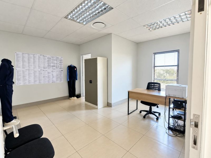 A clean, well-lit office space featuring neutral tiled flooring, a suspended ceiling with recessed lighting, and large windows with fitted blinds.