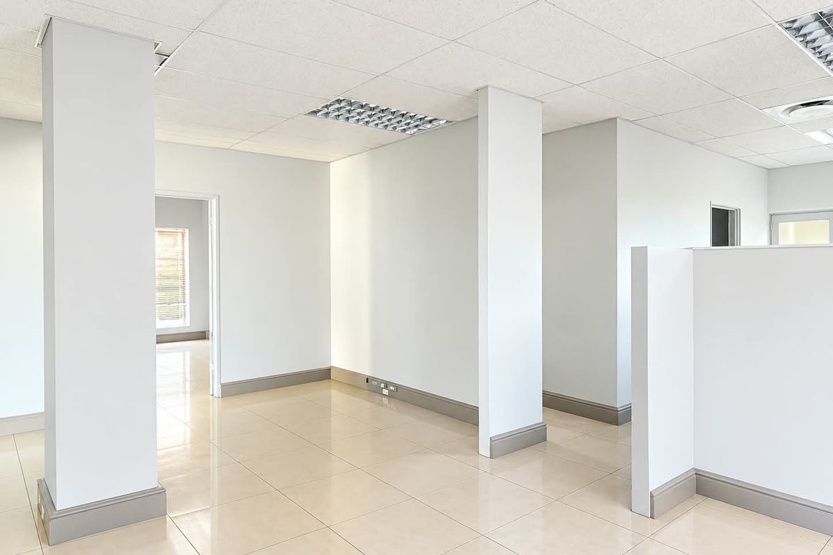 A bright, open-plan office space featuring neutral ceramic tile flooring, a suspended ceiling with recessed lighting, and clean, modern finishes throughout.