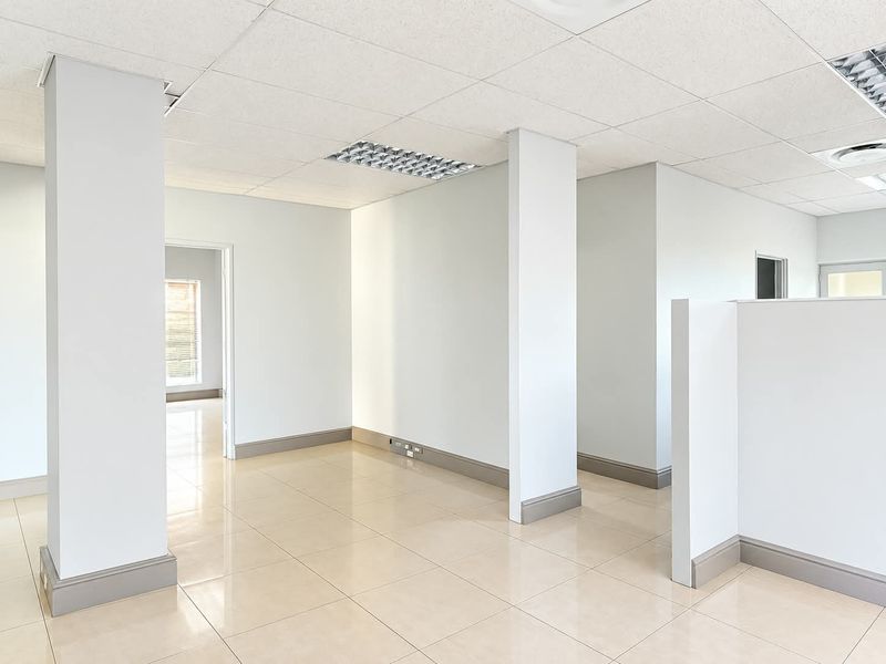 A bright, open-plan office space featuring neutral ceramic tile flooring, a suspended ceiling with recessed lighting, and clean, modern finishes throughout.