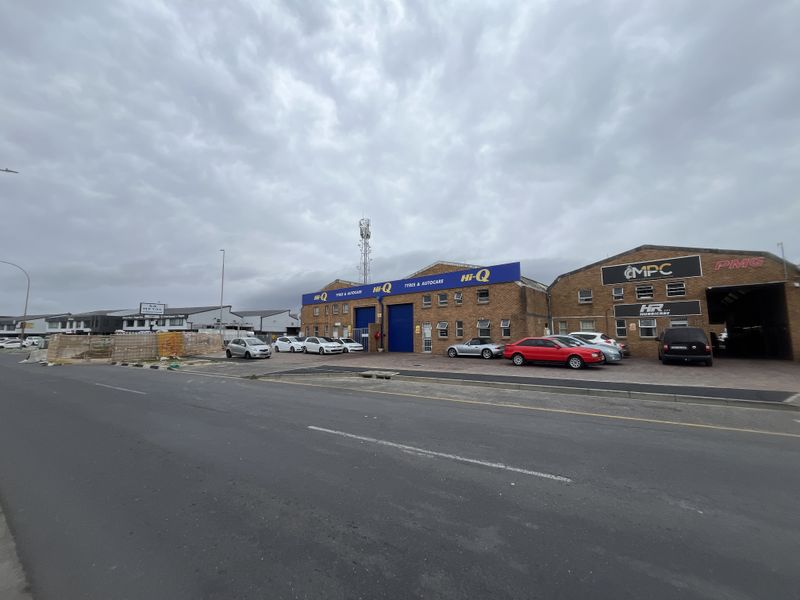 Front exterior view of an industrial warehouse complex featuring brick construction, large roller shutter access, and a paved forecourt area.