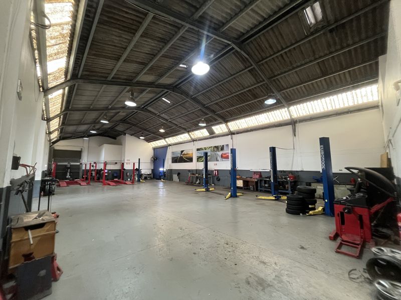 Spacious industrial workshop featuring multiple vehicle lifts, high-bay lighting, exposed steel roof structure, and durable epoxy-coated concrete flooring.
