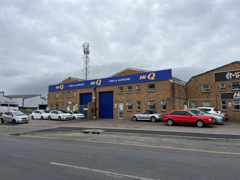 Front elevation of an industrial property featuring brick construction, large roller shutter doors, and prominent signage, situated on a paved forecourt.