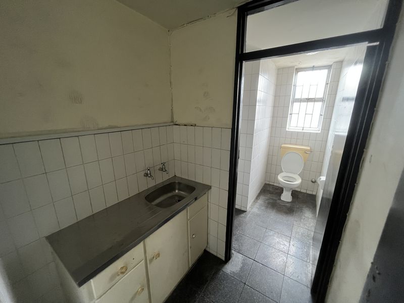 A dated bathroom and utility area featuring a stainless steel sink, built-in vanity, and separate toilet cubicle with tiled finishes.