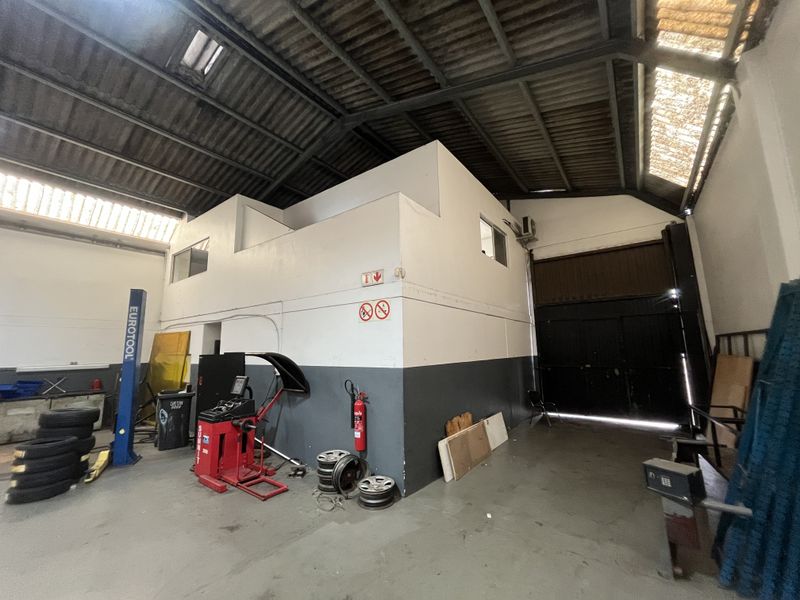 Spacious industrial garage featuring a mezzanine level, high ceilings with skylights, concrete flooring, and a large roller shutter door for vehicle access.
