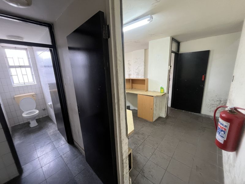 Industrial utility space featuring tiled flooring, built-in desk area, and an adjacent restroom, showing signs of wear and requiring cosmetic updates.