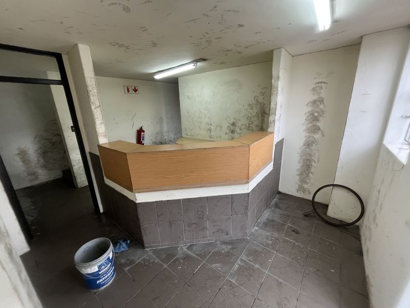 An industrial reception area featuring a built-in counter, tiled flooring, and fluorescent lighting, currently requiring cosmetic refurbishment and wall repairs.