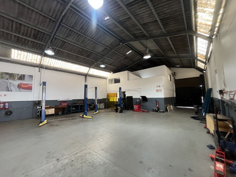 Spacious industrial workshop featuring high ceilings with exposed steel trusses, skylights, concrete flooring, and multiple built-in vehicle lifts for automotive operations.