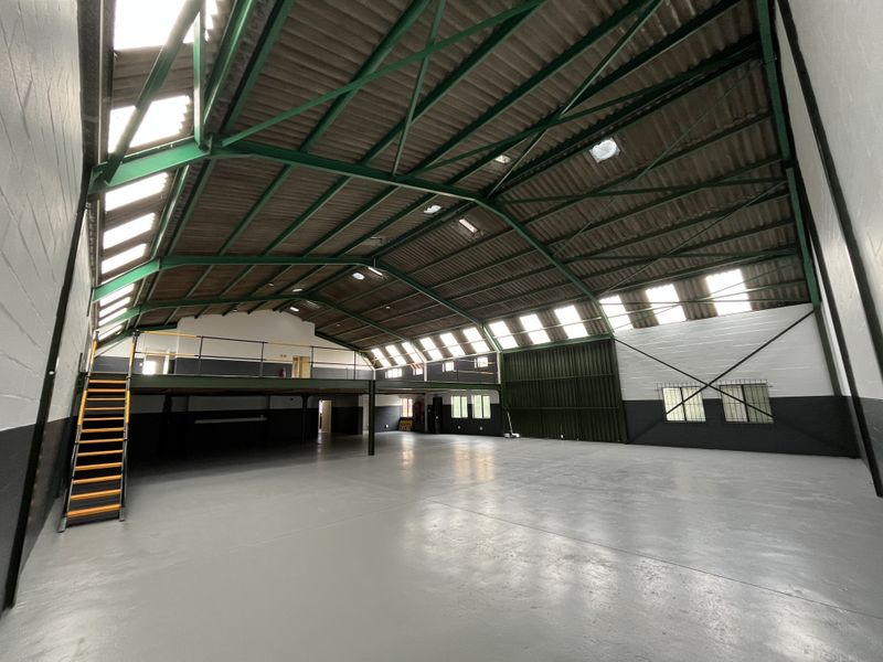 Spacious industrial warehouse featuring high ceilings with exposed steel trusses, abundant natural light from skylights, a mezzanine level, and durable epoxy-coated flooring.