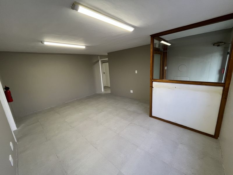 An empty industrial office space featuring tiled flooring, fluorescent lighting, and a partitioned glass wall divider.