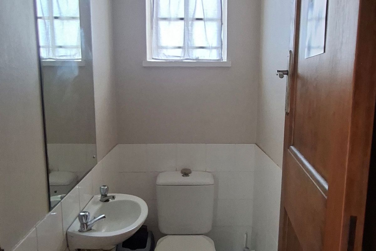 A functional bathroom featuring a pedestal basin, toilet, and tiled flooring, providing essential facilities for the office space.