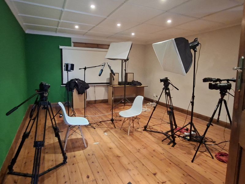 A functional office space currently utilized as a recording studio, featuring timber flooring, recessed lighting, and a dedicated green screen wall.