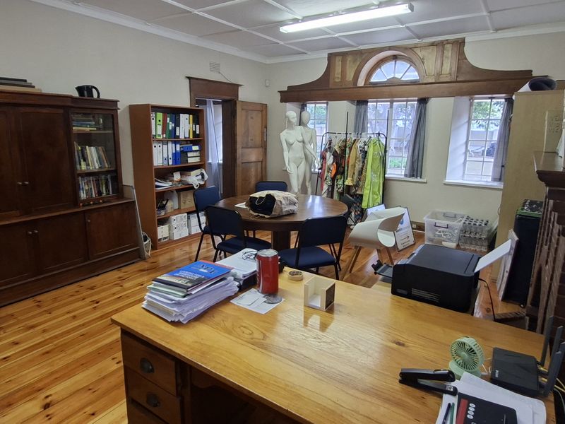 Spacious office featuring polished hardwood flooring, built-in wooden cabinetry, and a classic brick fireplace surround with arched window detailing.