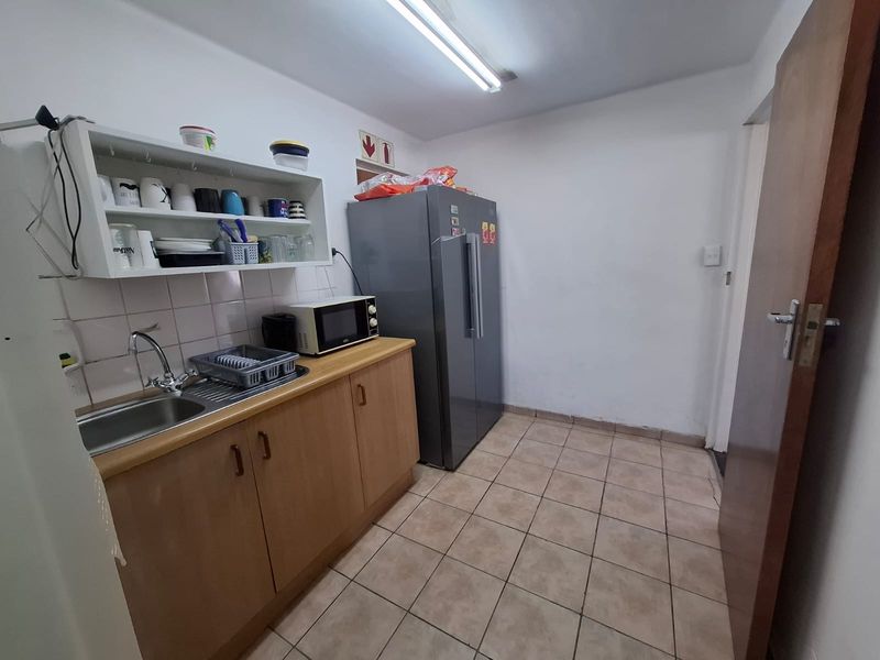 A functional scullery area featuring laminate cabinetry, a stainless steel sink, tiled splashback, and ceramic floor tiles.