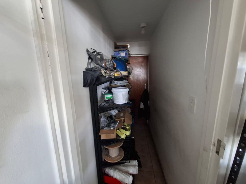 A narrow utility or storage corridor featuring tiled flooring and a solid core door, suitable for organized industrial storage or maintenance access.