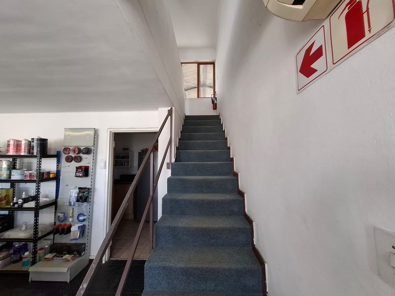 Interior view of a functional industrial hallway featuring a carpeted staircase with a metal handrail and essential safety signage.
