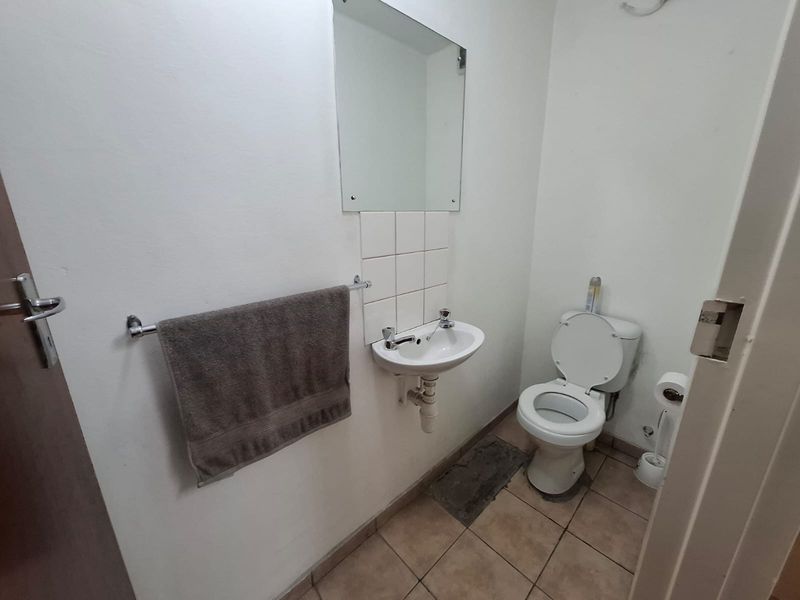 A functional industrial-style bathroom featuring a wall-mounted basin, toilet, and tiled flooring, presenting a basic and utilitarian space in need of cosmetic updates.