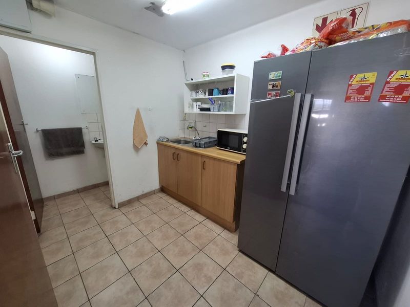 A functional kitchenette area featuring basic cabinetry, a stainless steel sink, and tiled flooring, with an adjacent small washroom.